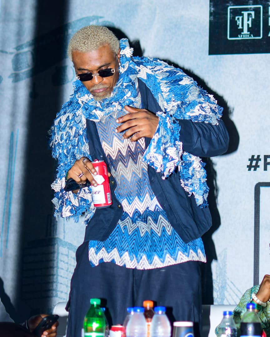 Guest in a blue knit look on stage against the Fashions Finest Africa backdrop
